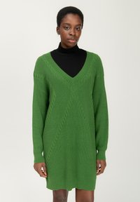 Abito lavorato a maglia verde con scollatura a V, maniche lunghe e modelli a treccia testurizzati. Tessuto morbido e spesso con una vestibilità rilassata, che arriva a metà coscia.