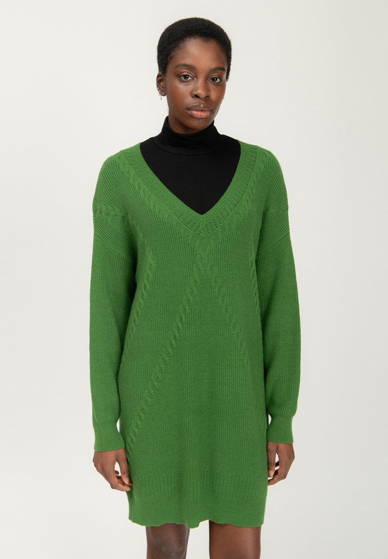 Abito lavorato a maglia verde con scollatura a V, maniche lunghe e modelli a treccia testurizzati. Tessuto morbido e spesso con una vestibilità rilassata, che arriva a metà coscia.