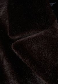 Svart konstpäls med en mjuk, strukturerad yta och glänsande detaljer samt ett slätt, lager-på-lager utseende.
