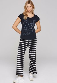 Navy short-sleeve top with white graphic text paired with black-and-white striped wide-leg pants. White athletic shoes complete the outfit.