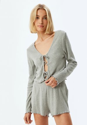 Helles graues Ripp-Loungewear-Set mit V-Ausschnitt, Krawattenverschluss und Rüscheärmel, kombiniert mit kurzen Hosen und seitlichen Taschen.