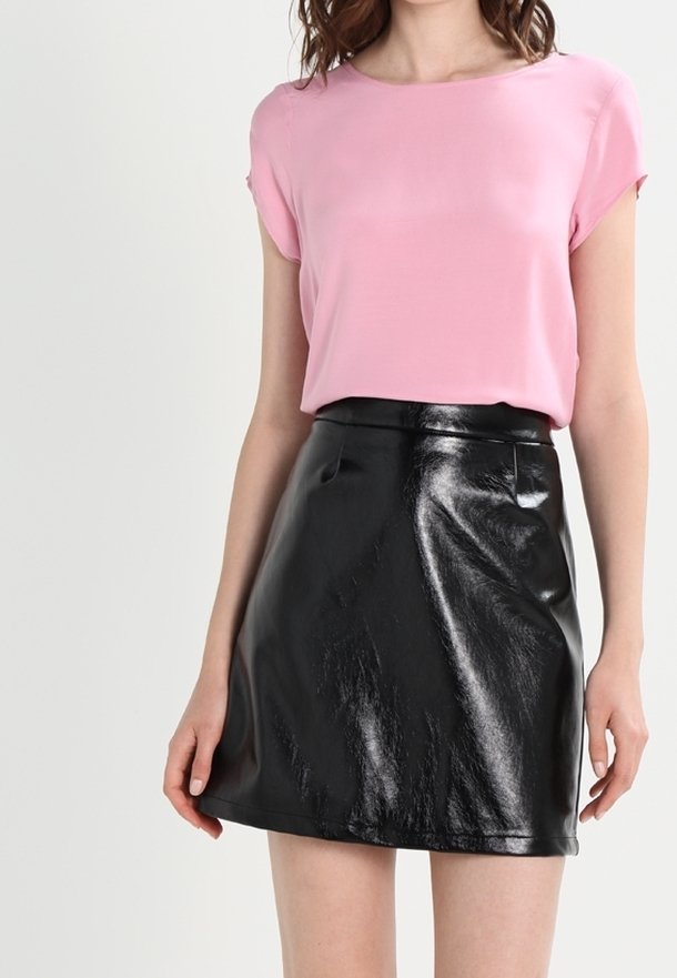 Haut rose à manches courtes associé à une mini-jupe taille haute en similicuir noir. La jupe a une texture brillante et un design minimaliste.