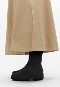 Zwarte platformlaarzen met een gladde textuur, voorzien van een strak ontwerp en een uitgerekte vorm, gecombineerd met een lichtbeige rok tot de knie.