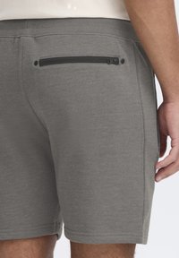Des shorts gris en tissu doux présentent une poche latérale zippée et une texture lisse, avec des ourlets surpiqués et une coupe décontractée.