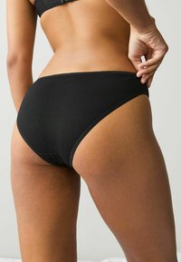 Juodos medvilnės bikini kelnaitės su sklandžiu paviršiumi, vidutinio aukščio kirpimu ir kontrastingomis siūlėmis juosmens ir kojų angose.