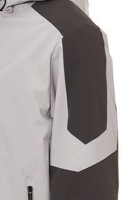 Waterdichte jas met een grijs lichaam en zwarte accenten. Beschikt over een ritszak, een aangesloten capuchon en een patchdetail op de schouders.