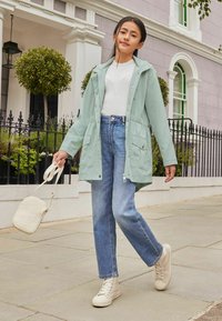 Ljusgrön, huva-jacket med tryckknappar, bärs över en vit ribbad tröja och högmidjade blå jeans. Beige sneakers och liten väska.