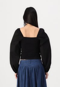 Haut noir à manches bouffantes avec des détails froncés, un dos carré et une taille ajustée, assorti à une jupe en denim présentant une texture froncée et des coutures.