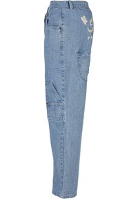 Pantalon cargo en denim bleu clair avec poches latérales à rabat et texte et motif blancs brodés près de la hanche, vu de côté gauche.