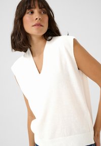 Débardeur blanc sans manches en tissu tricoté doux, avec un ourlet côtelé et une coupe décontractée au design minimaliste.