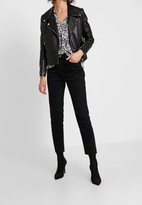 Giacca da biker in pelle nera sopra una blusa bianca e nera con stampa leopardata, abbinata a jeans skinny neri e stivaletti con tacco.