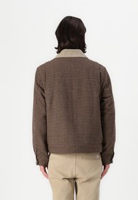 Chaqueta a cuadros marrón y beige con cuello, que presenta mangas largas y puños abotonados. Tejido suave, diseño corto y corte relajado.