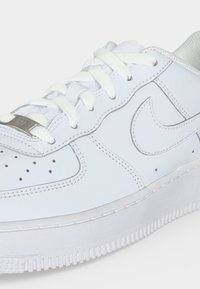 Gros plan d'une chaussure de sport en cuir blanc avec lacets blancs, zone des orteils perforée, détails cousus et semelle en caoutchouc.