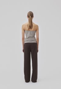 Top gris sin mangas combinado con pantalones de pierna ancha marrón oscuro, que exhiben una textura suave y un diseño minimalista. Vista trasera, fondo liso.