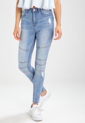 Světle modré džíny skinny s distressed detaily a švy, s vysokým pasem a upnutým střihem, doplněné o bílé tenisky.
