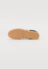 Semelle de sneaker textile noire avec un fond en caoutchouc gomme. Présente un motif en chevrons et des détails circulaires. Texte "adidas" estampé sur le côté.