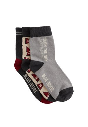 Tre par av strumpor i crew-stil i grå, mörkgrå och vinröd. Mönster inkluderar geometriska designer och text, tillverkade av mjukt strickmaterial.