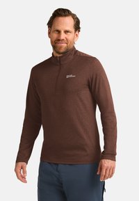 Brauner Pullover mit langen Ärmeln und einem halben Reißverschluss-Kragen, aus strukturiertem Stoff. Mit einem kleinen Logo auf der oberen linken Brust.