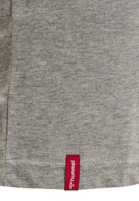 Grå bomull T-shirt med en slät textur. Har en röd vävd etikett med "hummel" vid fållen. Enkel, avslappnad design.