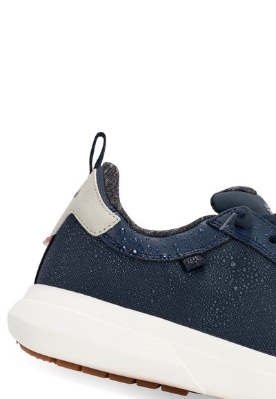 Zapatilla azul marino con tejido resistente al agua, panel lateral texturizado, acento gris cerca del talón y suela blanca con tracción marrón.