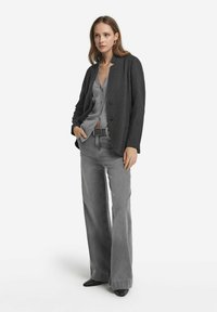 Szary teksturowany żakiet z okrągłym kołnierzem i zapięciem na guzik, nałożony na szary top. Połączony z szarymi dzwonami i czarnymi butami.