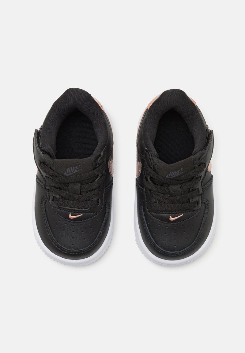 Baskets en cuir noir avec semelles blanches, dotées de lacets, d'un bout perforé et d'un petit logo Swoosh Nike en rose gold sur les côtés.