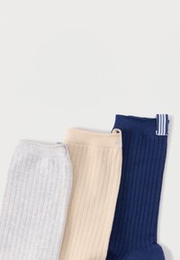 Três pares de meias caneladas: cinza claro, bege e azul-marinho. Cada meia apresenta um punho contrastante com um padrão sutil de riscas.