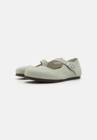 Zapatos Mary Jane de ante verde con punta redonda, correa alrededor del tobillo y suela marrón texturizada. Presentan un diseño recortado en el lateral.