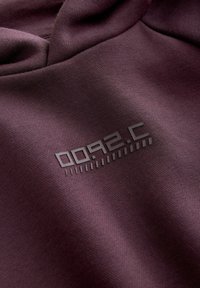 Gros plan sur un tissu violet foncé avec un petit motif imprimé noir composé de formes géométriques et de lignes.