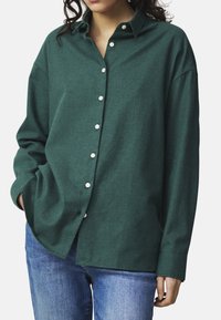 Dunkelgrünes Hemd mit Knöpfen, aus strukturiertem Stoff und mit lässiger Passform, ausgestattet mit einem klassischen Kragen und weißen Knöpfen. Trägt man über Jeans.