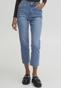 Jeans de mezclilla azul de tiro alto con corte recto y dobladillo desflecado. Llevados con mocasines negros que cuentan con acentos de hardware dorado.