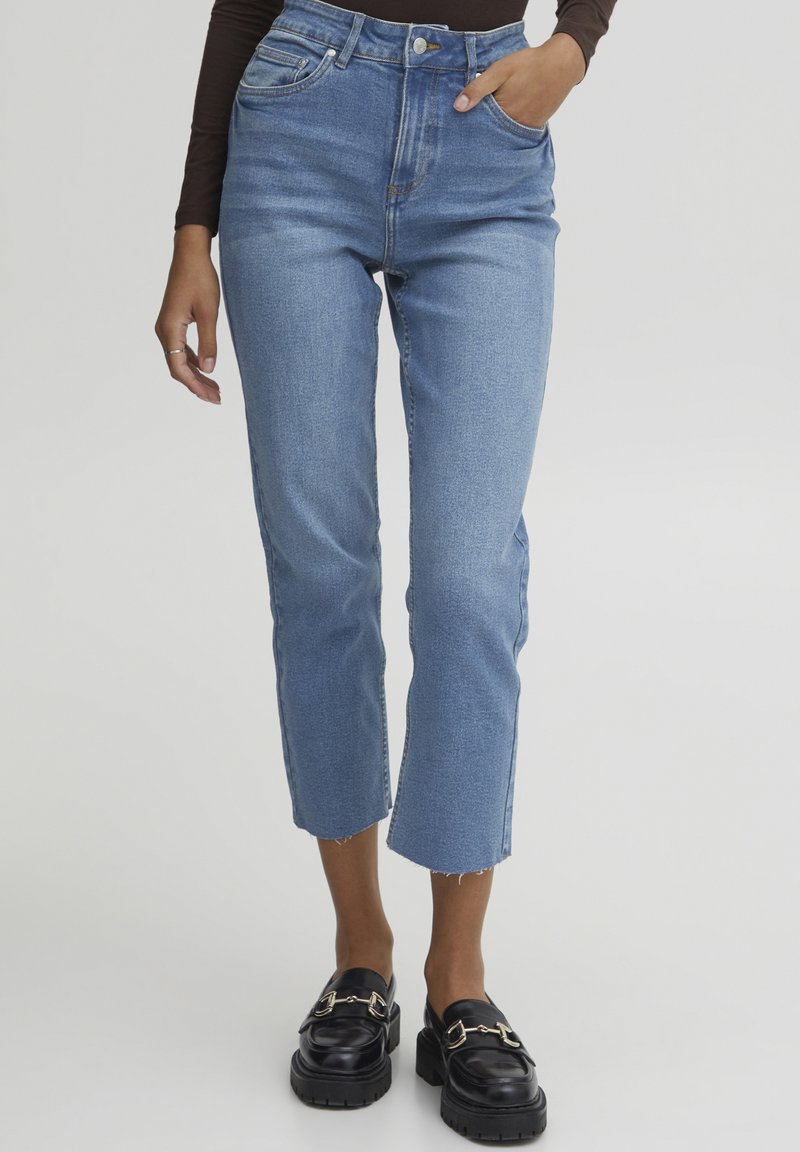 Jeans de mezclilla azul de tiro alto con corte recto y dobladillo desflecado. Llevados con mocasines negros que cuentan con acentos de hardware dorado.