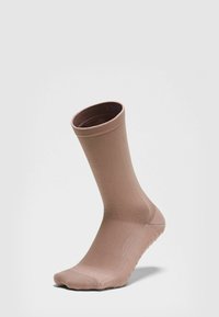 Šviesiai ruda kulkšnies atrama kojinė su tekstūruota padu, sukurta suspaudimui ir sukibimui, stovinti vertikaliai ant lygaus šviesaus fono.