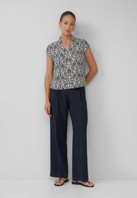 Blouse à manches courtes avec un motif de feuilles bleu marine et crème, associé à un pantalon large bleu marine et des sandales noires. Texture de tissu lisse.