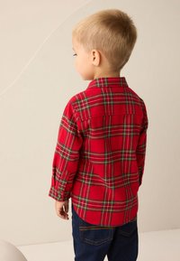 Camicia di flanella a quadri rossi con accenti verdi e gialli, caratterizzata da un colletto con bottoni e maniche lunghe. Indossata con jeans blu scuro.