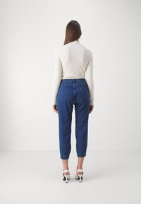 Pantaloni cropped in denim blu con taglio dritto, dotati di vita alta, tasche laterali e orli risvoltati, abbinati a un maglione a coste color crema.