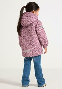 Roze jas met bloemenpatroon en capuchon, voorzien van reflecterende accenten en elastische manchetten, gedragen met blauwe jeans. Achteraanzicht.
