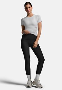 Czarne legginsy z wysokim stanem w połączeniu z dopasowanym białym T-shirtem i jasnymi trampkami. Gładka tkanina o eleganckim designie.