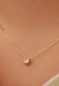 Gouden ketting met een fijne schakel en een ronde hanger, met een heldere edelsteen in een gladde zetting. Achtegrond van textuur huid.