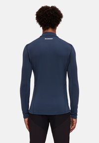 Marineblaue langärmelige Sportshirt mit hohem Kragen und reflektierendem Logo auf dem Rücken. Hergestellt aus glattem, leichtem Stoff mit flachen Nähten.