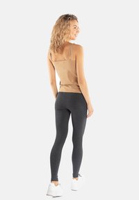Beżowy top na ramiączkach zestawiony z ciemnoszarymi legginsami. Materiał wydaje się miękki, ma dopasowany krój i gładką teksturę.