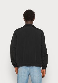 Svart bomberjacka med en smidig yta, ribbade muddärmar och en kroppsnära nederdel, utformad med en klassisk krage och minimalistisk design.