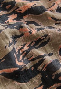 Geweven stof met een tijgerstreepdesign in zwart en roestoranje op een licht beige achtergrond, met een getextureerd oppervlak.