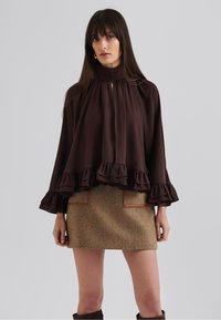 Blouse marron à volants avec un col haut et des détails de boutons, associé à une mini-jupe texturée marron avec des accents beiges.