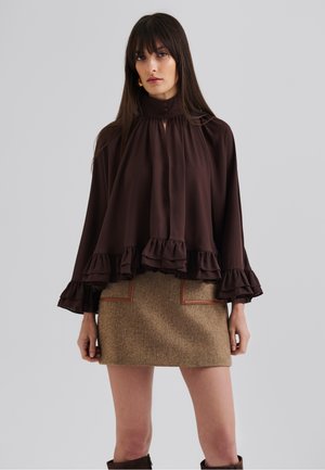 Bruine ruffle blouse met een hoge kraag en knoopdetails, gecombineerd met een textuurrijke bruine minirok met beige accenten.
