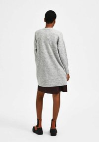 Abito in maglia grigio con vestibilità comoda, maniche lunghe e schiena leggermente allungata. Abbinato a stivali alla caviglia neri e arancioni.