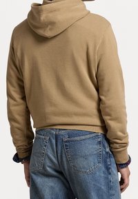 Felpa con cappuccio in cotone beige con design corto, abbinata a jeans di denim blu chiaro con due tasche posteriori e cuciture visibili.