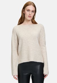 Hellbeige gestrickter Pullover mit Rundhalsausschnitt, langen Ärmeln, strukturiertem Stoff und einem etwas verkürzten Saum. Wird mit schwarzen Hosen kombiniert.