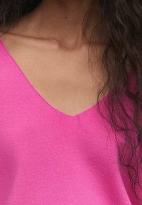 Pinkes V-Ausschnitt-Strickoberteil mit glatter Textur, figurbetonter Silhouette und sauberer Naht am Halsausschnitt, geeignet für legere Kleidung.