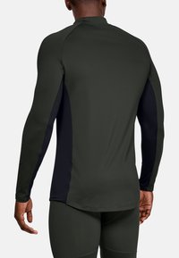 Hombre vistiendo una camiseta deportiva ajustada de manga larga en verde oscuro con paneles laterales negros y leggings a juego, visto desde la espalda.